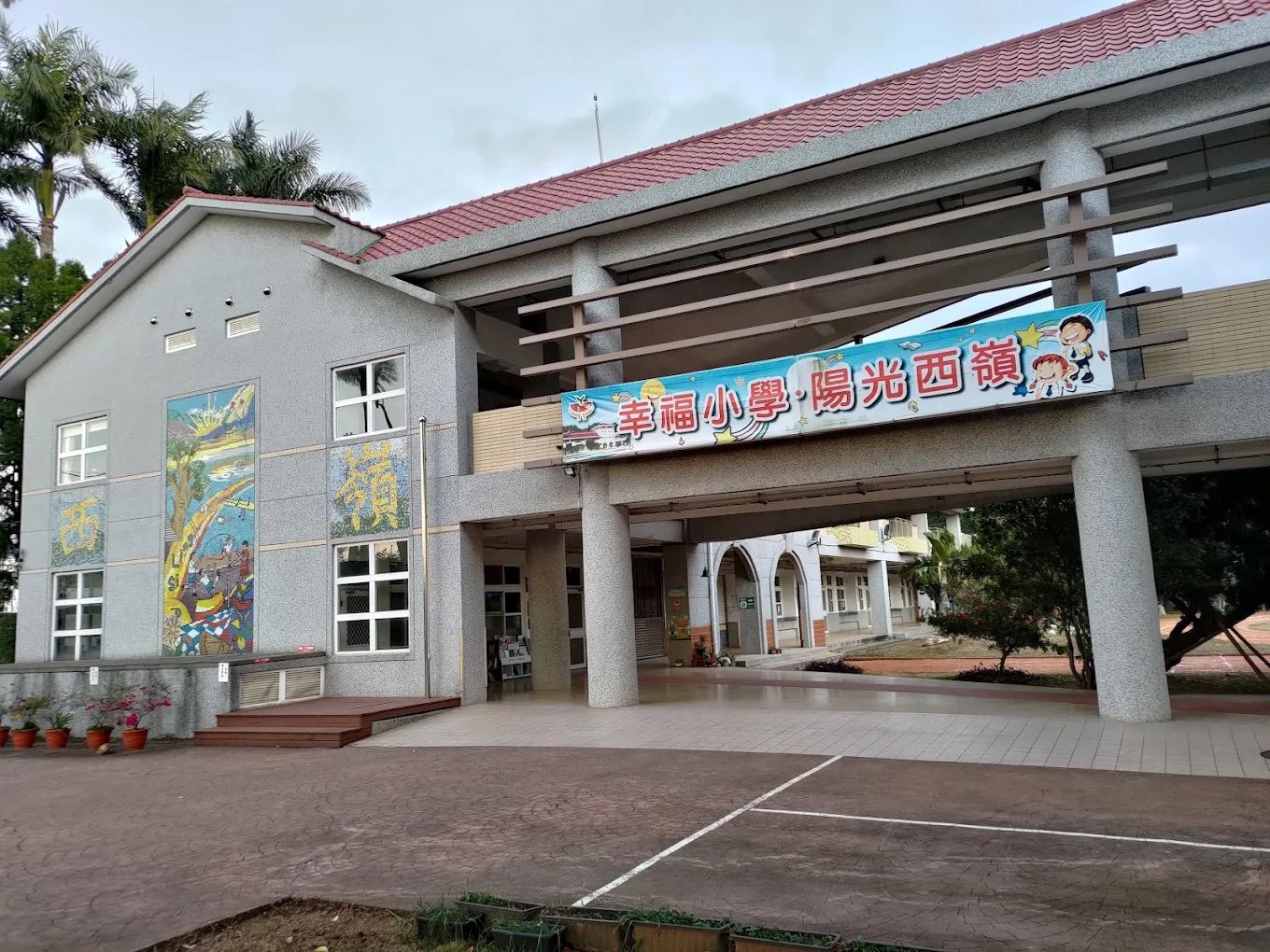 西嶺國小穿堂前掛著「幸福小學.陽光西嶺」布條,牆面彩繪壁畫 A banner reading 'Sunny Siling' hangs at the school's entrance hall, beside a colourful mural