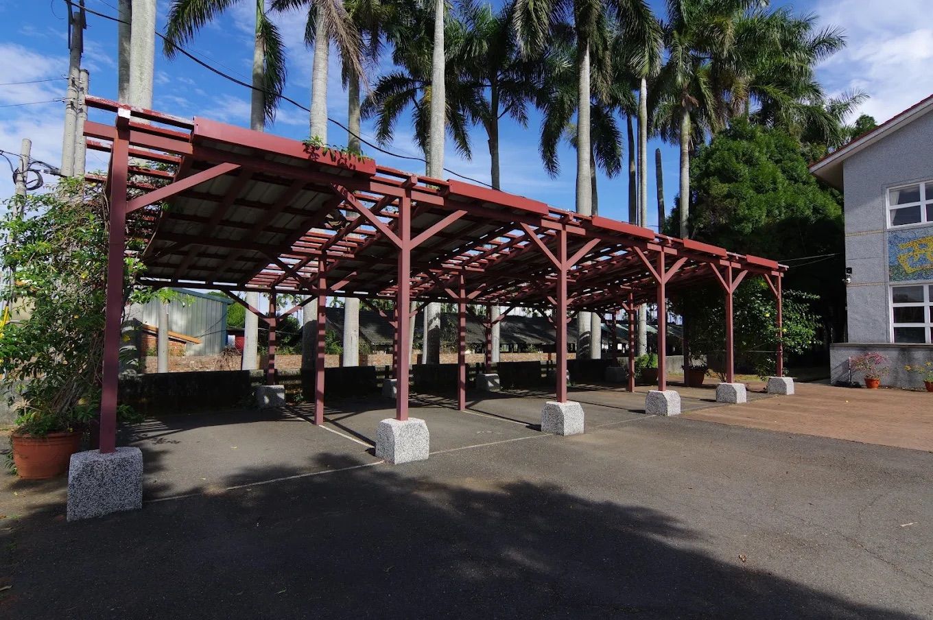 西嶺國小紅色風雨走廊,兩側高聳的大王椰子樹,藍天白雲 A red-framed covered walkway lined with tall royal palms under a blue sky