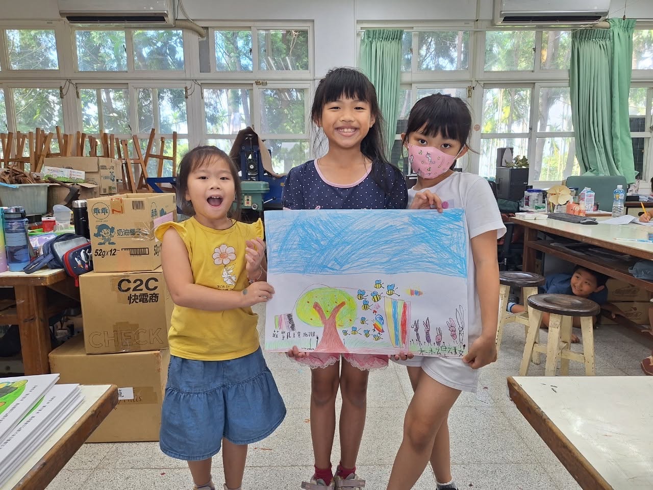 三位西嶺國小學生開心地展示他們共同完成的彩色畫作 Three Siling students happily hold up a colourful painting they made together