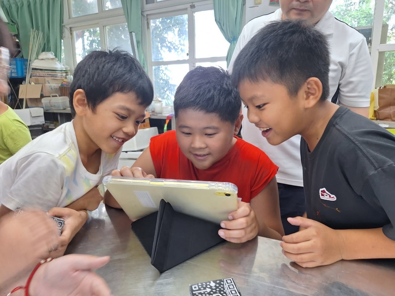 三位西嶺國小學生開心地圍著平板電腦一起學習 Three Siling students gather happily around a tablet to learn together