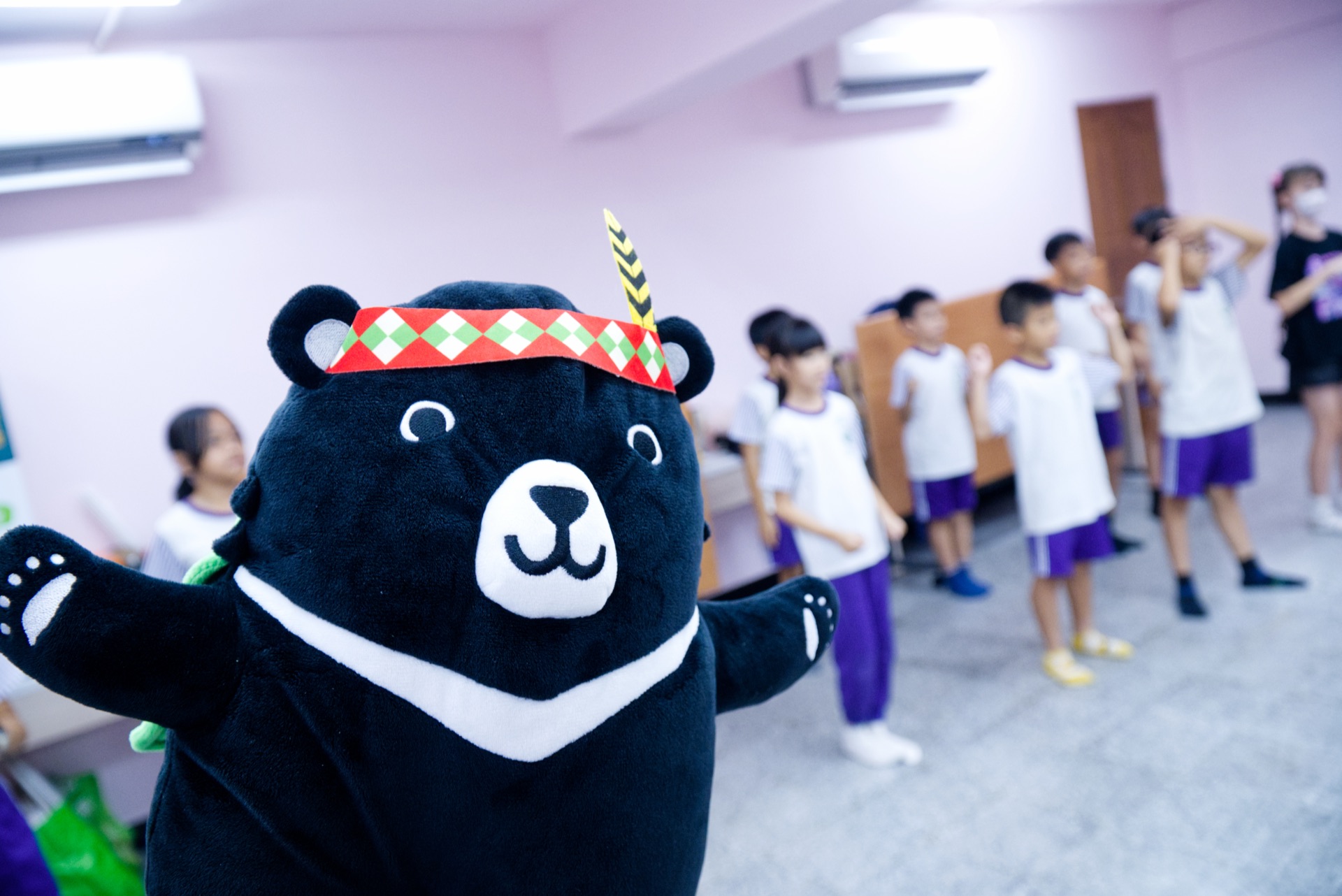 The SDG bear mascot poses as campers rehearse dance steps in the background